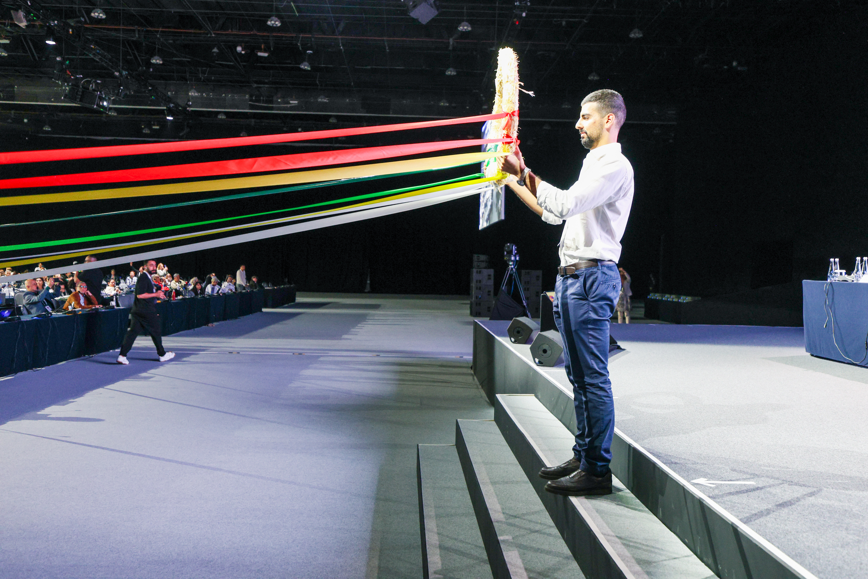 Man holds up large circle from which ribbons extend towards the audience