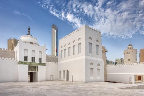 The main gate of Qasr Al Hosn on a sunny day against a backdrop of clear blue skies and puffy clouds, featuring the Qasr Al Hosn fort and watchtower.